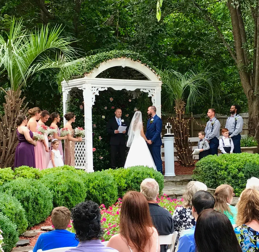 Exchanging vows at the garden arbor as guests watch