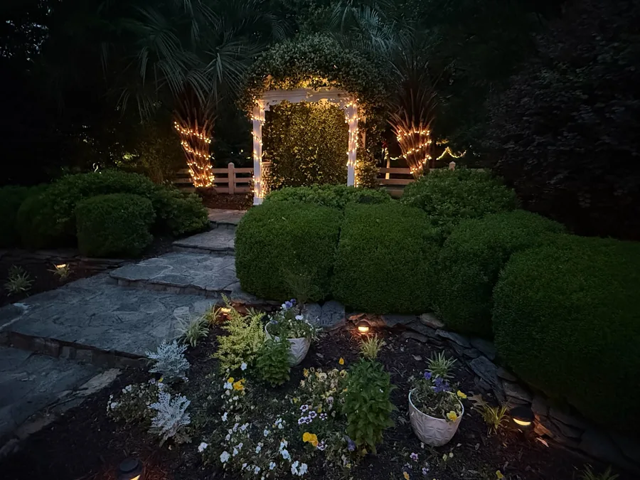 Garden ceremony setting with stone paver path and lit arbor