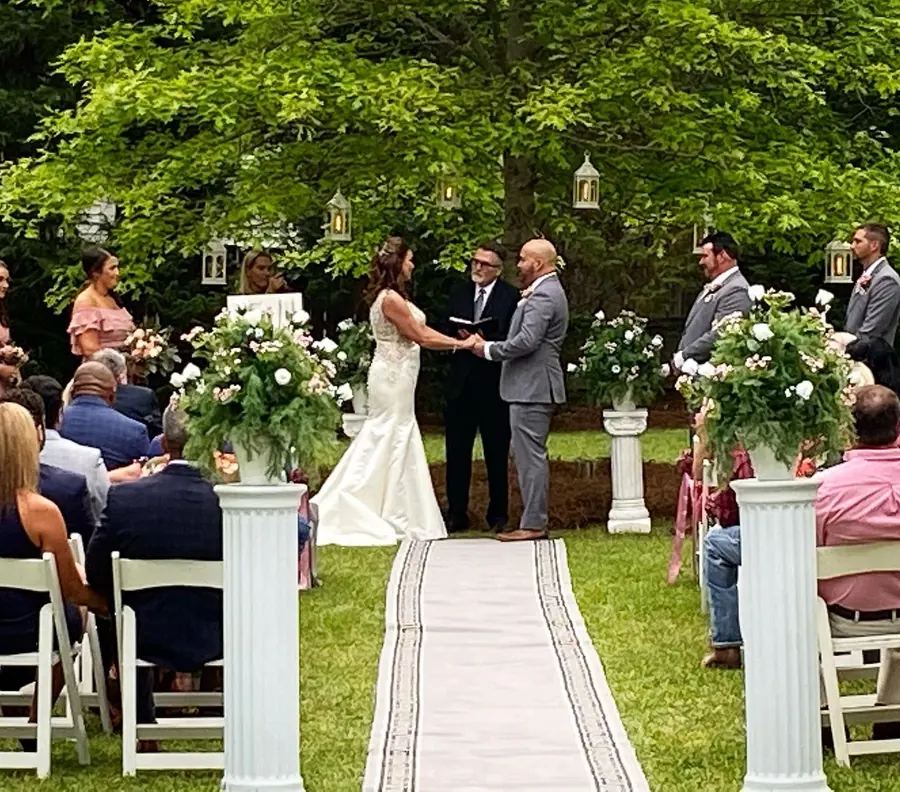 Lawn ceremony with a white aisle runner and floral pillars